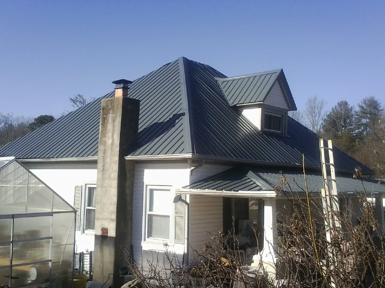 Dark blue standing seam metal roof on a white farmhouse with dormer — Slate & Tile Roof Repair by Roofing Brothers in Byfield