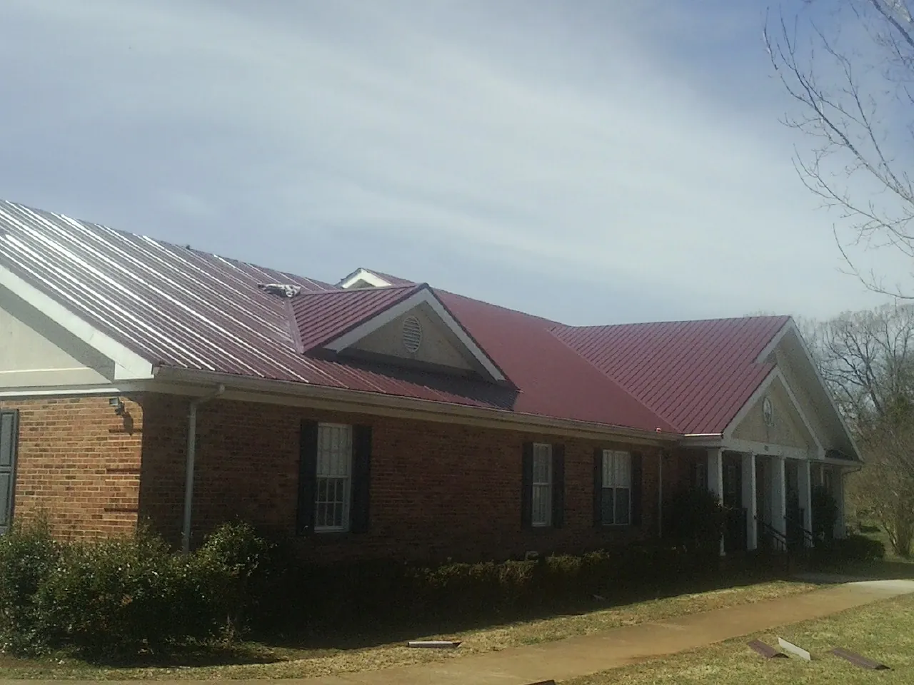 Red metal roof with gabled entries on a long brick building, from a Hail Damage Roof Repair job in Byfield