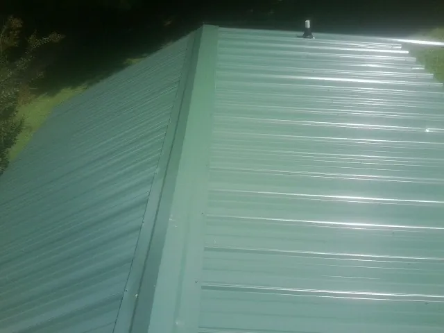 New green metal panels meeting at the ridge of a roof — Flat Roof Repair work by our crew in Byfield