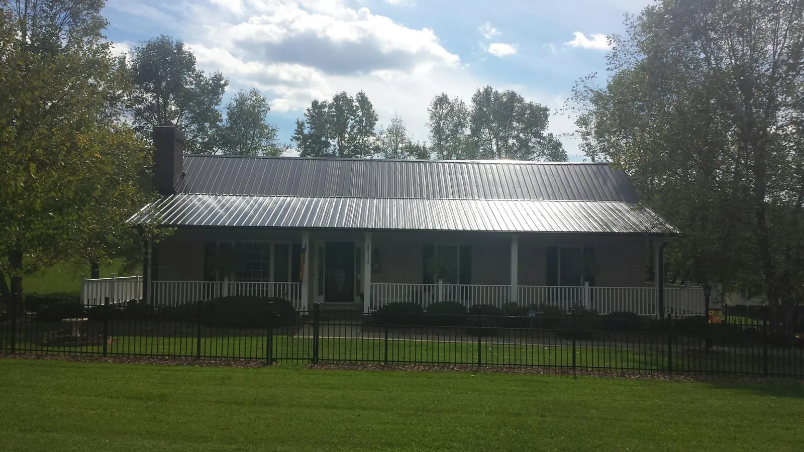 Gray metal roof on a brick ranch with a full width front porch — Gutter Guard Installation work by our crew in Byfield