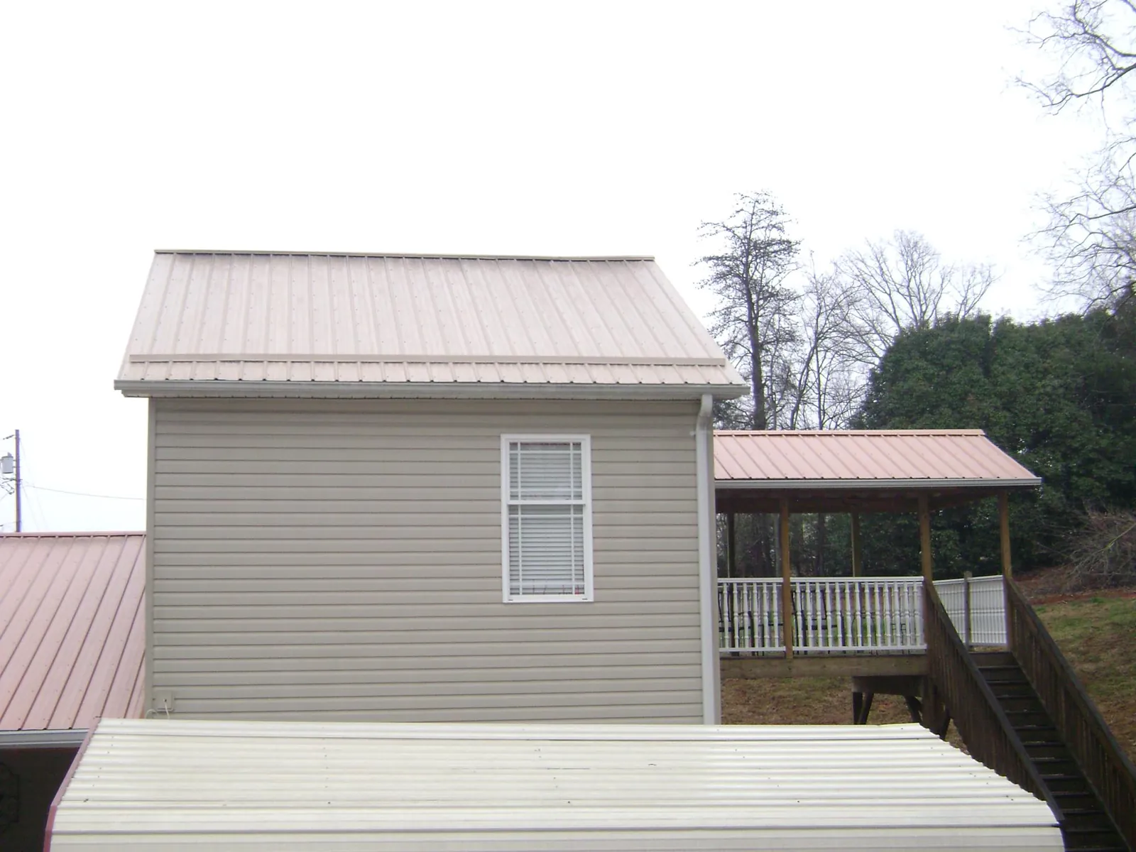 Tan metal roofs on a two story addition and attached porch, from a Roof Replacement job in Byfield